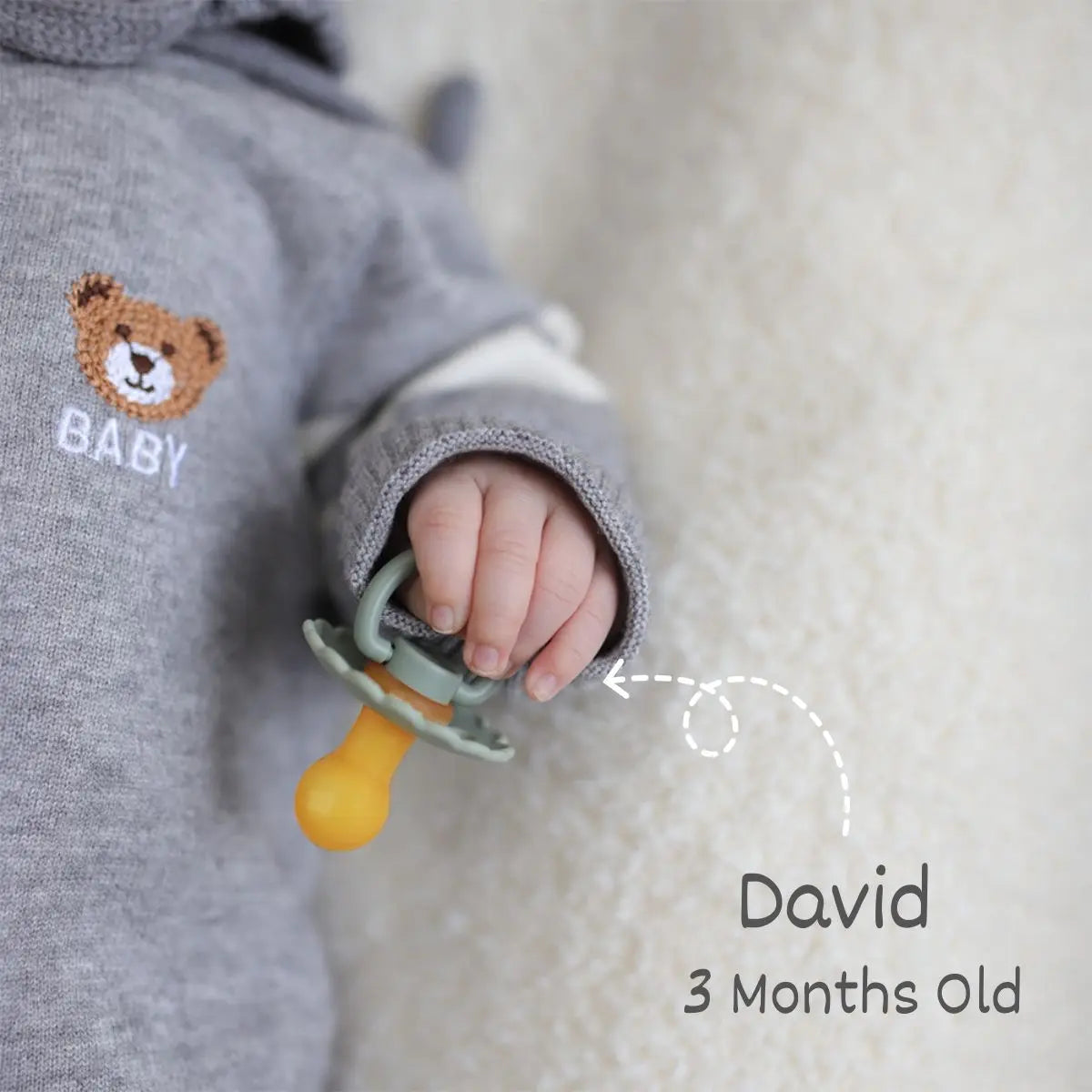 A baby's hand is holding a yellow natural latex pacifier against a soft, light-colored background.