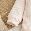 A light pink knitted baby romper and pants set lying on a beige textured surface.