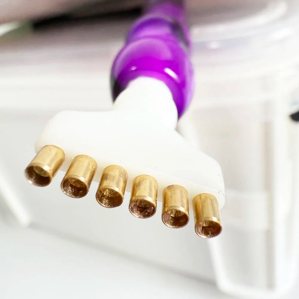 A close-up of a diamond painting pen set with interchangeable gold tips and a purple pen tip resting on a white surface.