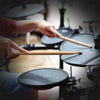 A pair of maple wood drumsticks being held by a person above a drum surface.