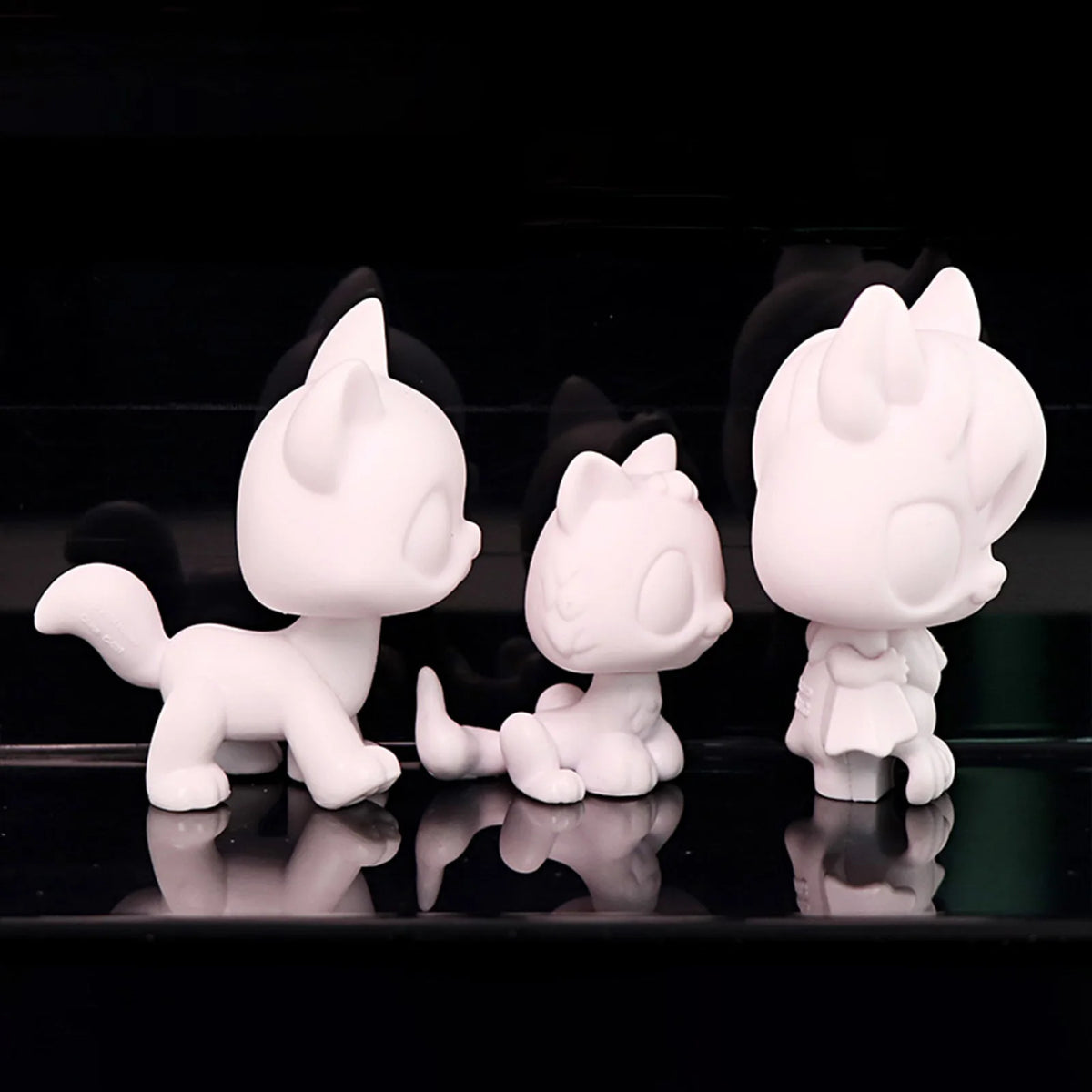 Three white printable bobble head figurines displayed against a black reflective surface.
