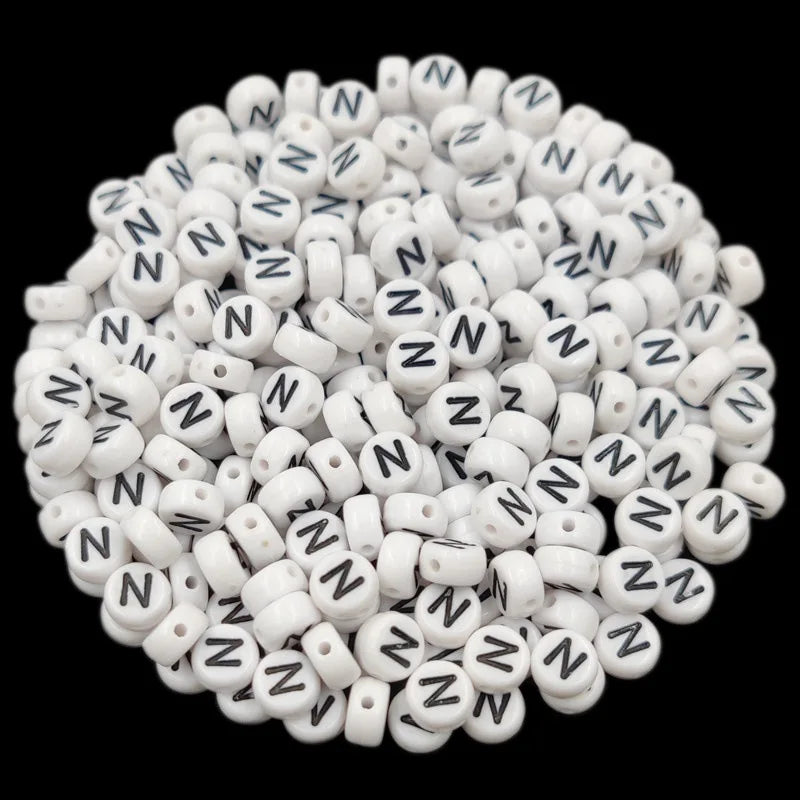 A pile of small white acrylic alphabet letter beads for jewelry making