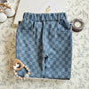 A pair of blue plaid corduroy pants with an elastic waist are displayed on a light patterned fabric.
