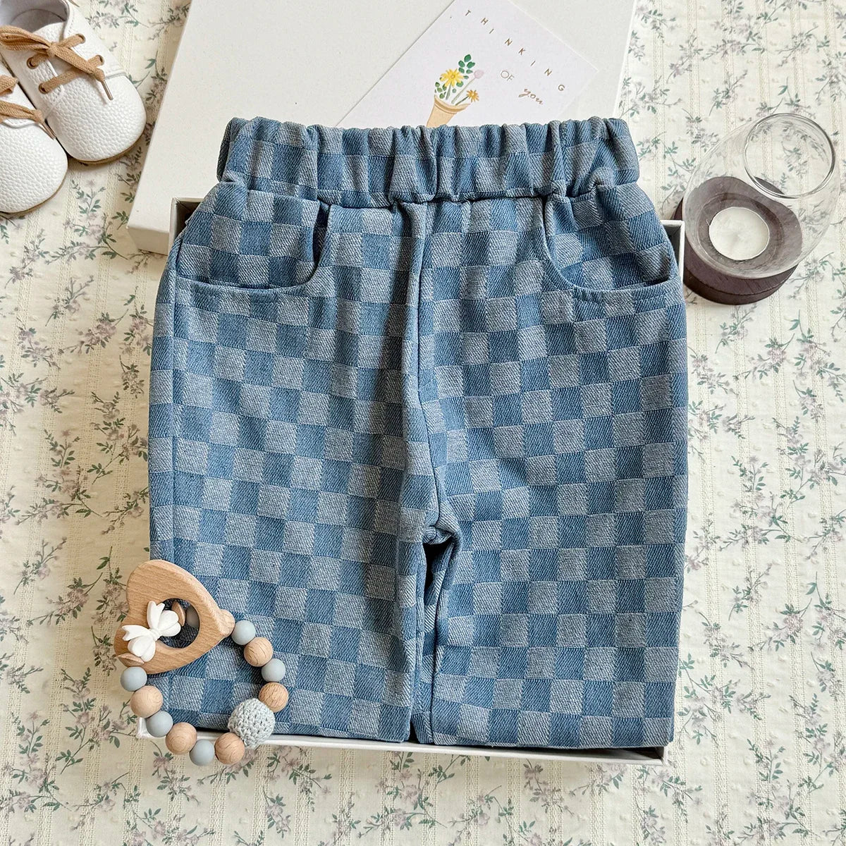 A pair of blue plaid corduroy pants with an elastic waist are displayed on a light patterned fabric.