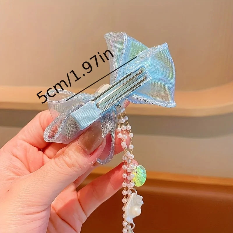 A hand holds a light blue mermaid princess hair clip featuring a butterfly design and pearl accents.