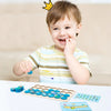 A smiling toddler holds a wooden memory chess game and matching tiles on a white surface.