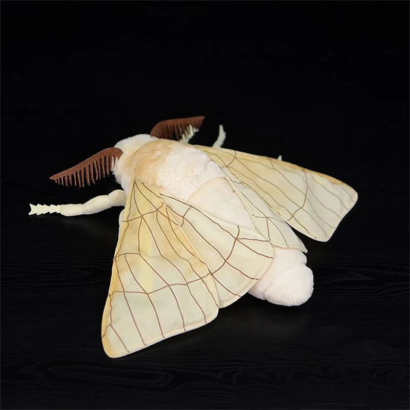 A soft, white silk moth plushie with delicate wings and fuzzy body is displayed against a dark background.