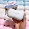 A hand holds a white soap-shaped squishy stress relief toy next to a row of similar toys.