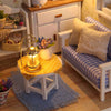 A miniature dollhouse puzzle kit with furniture sits on a yellow cloth next to a glowing lantern.