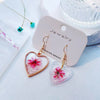 Gold-plated heart-shaped earrings with pink and gold floral designs displayed on a white background.