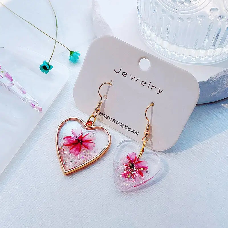 Gold-plated heart-shaped earrings with pink and gold floral designs displayed on a white background.