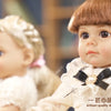A close-up of a realistic 4D process baby doll with brown hair and a white outfit.