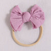 A light pink fabric bow headband with a beige elastic band, suitable for a baby or girl.