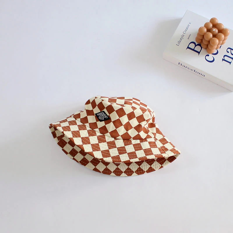 A terracotta and white checkered bucket hat resting on a white surface next to a book.