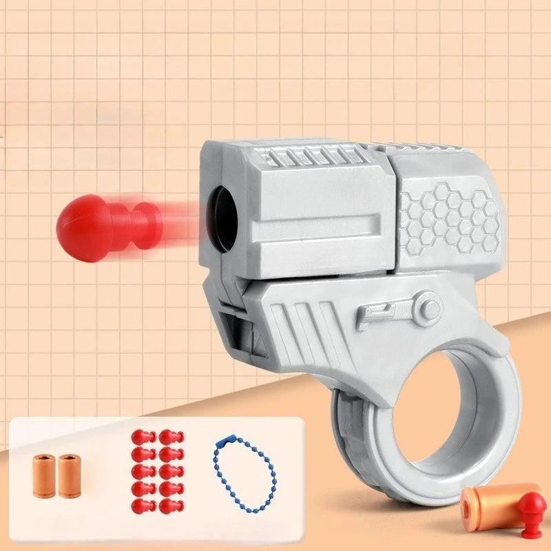 A silver mini shell-ejecting fidget pistol is shown next to various colored and metallic cartridges on a light background.