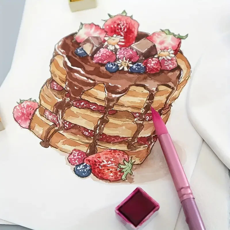 A stack of strawberry and berry decorated pancakes with chocolate drizzle on a white surface next to a pink brush pen.