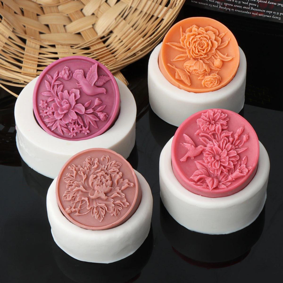 Three silicone molds shaped like peony flowers in pink and orange colors displayed on a dark surface.