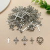 A collection of vintage silver cross charms and pendants for jewelry making scattered on a light background.