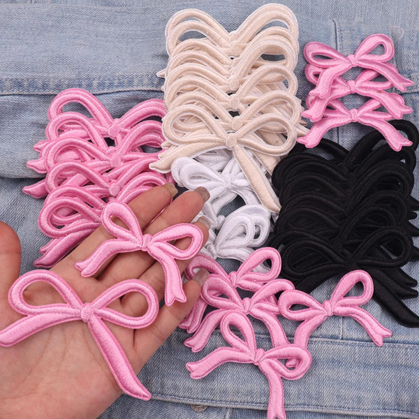 A collection of pink, white, and black embroidered ribbon bows for iron-on patches.