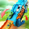 A blue dinosaur transport truck toy set with orange and yellow die-cast cars on a green grassy surface.