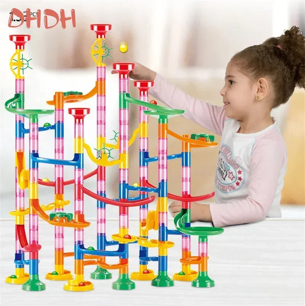 A young girl is playing with a colorful marble run building block set featuring various colored tubes and tracks.