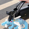 A hand is holding a black bag with a silver charm and a light blue rainbow dragon plush toy.