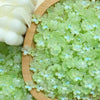 A pile of light green sakura flower crystal glass beads for jewelry making next to a white object.