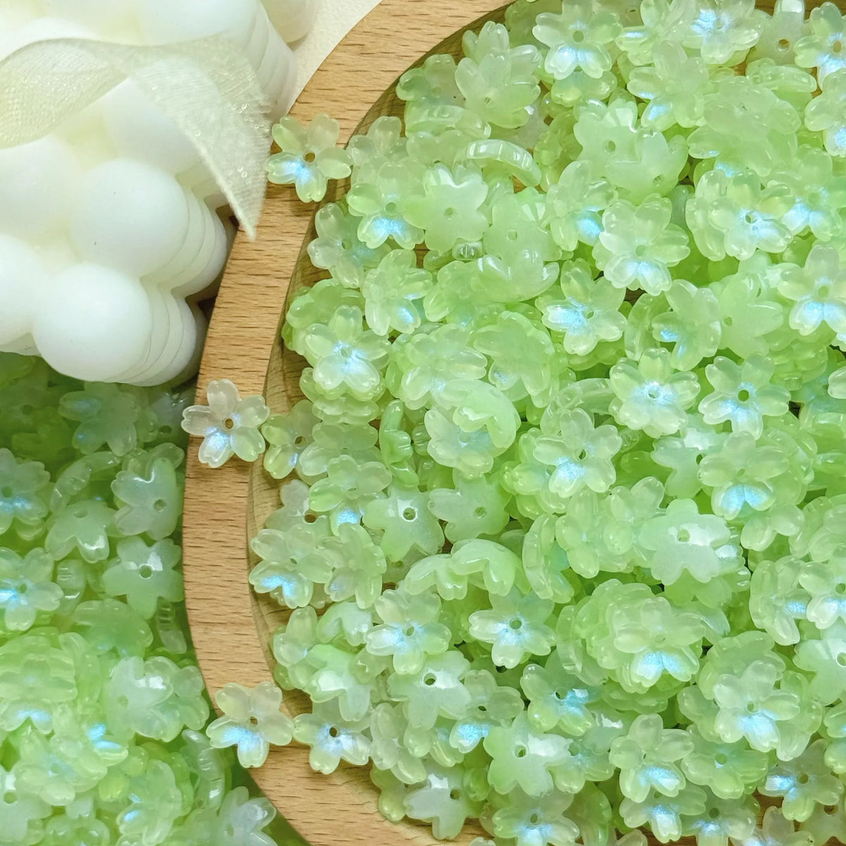 A pile of light green sakura flower crystal glass beads for jewelry making next to a white object.