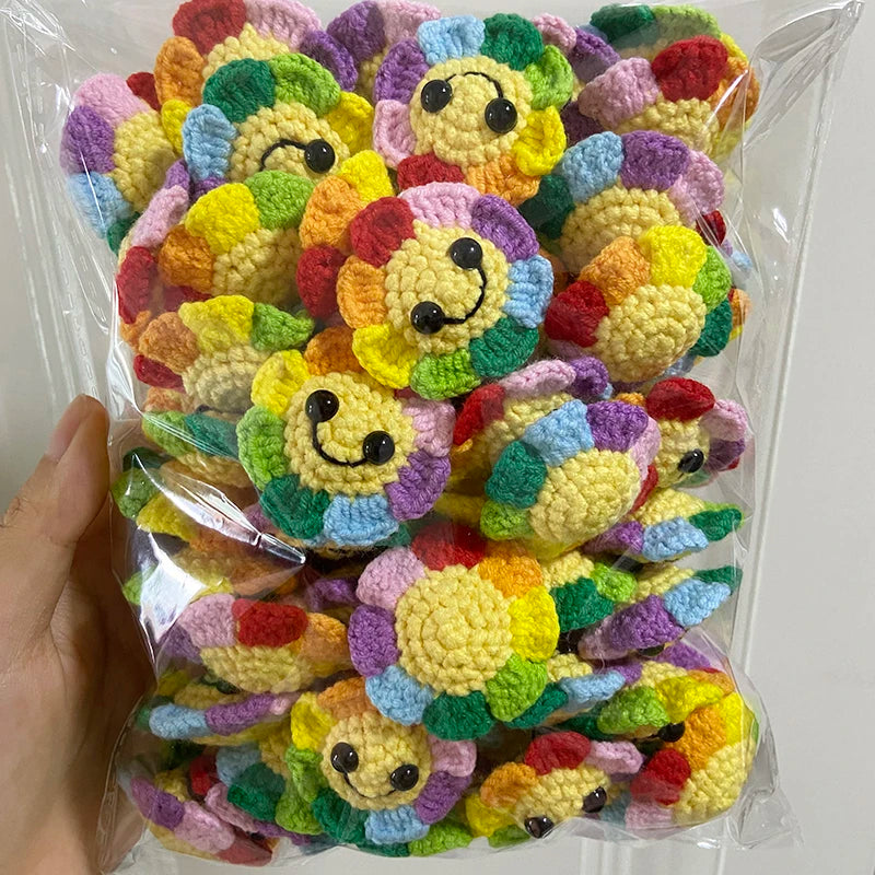 A hand holds a clear plastic bag filled with numerous handmade crochet sunflower decorative smile orbs in various bright colo