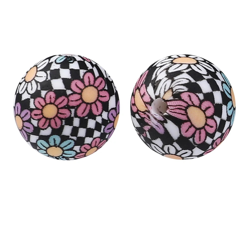 Two spherical silicone beads featuring a black and white checkered pattern with pink and blue floral designs.