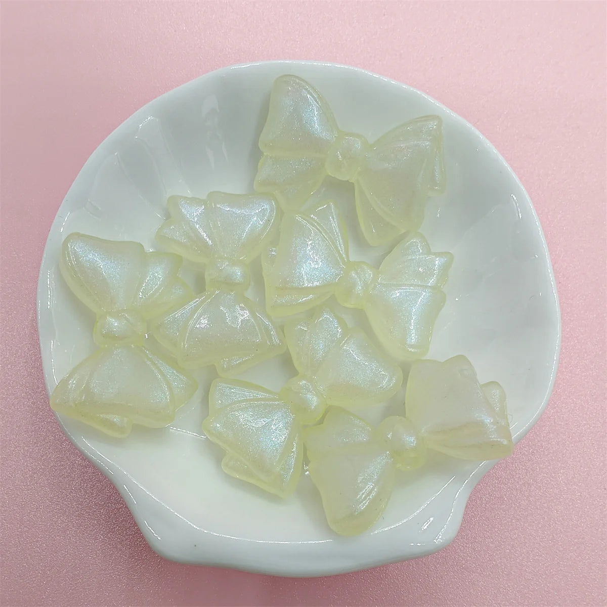 A collection of translucent pale yellow shimmer mermaid bowknot beads displayed in a white dish.