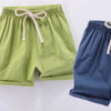 A pair of light green cotton-linen summer shorts with a beige drawstring, next to a pair of dark blue shorts.