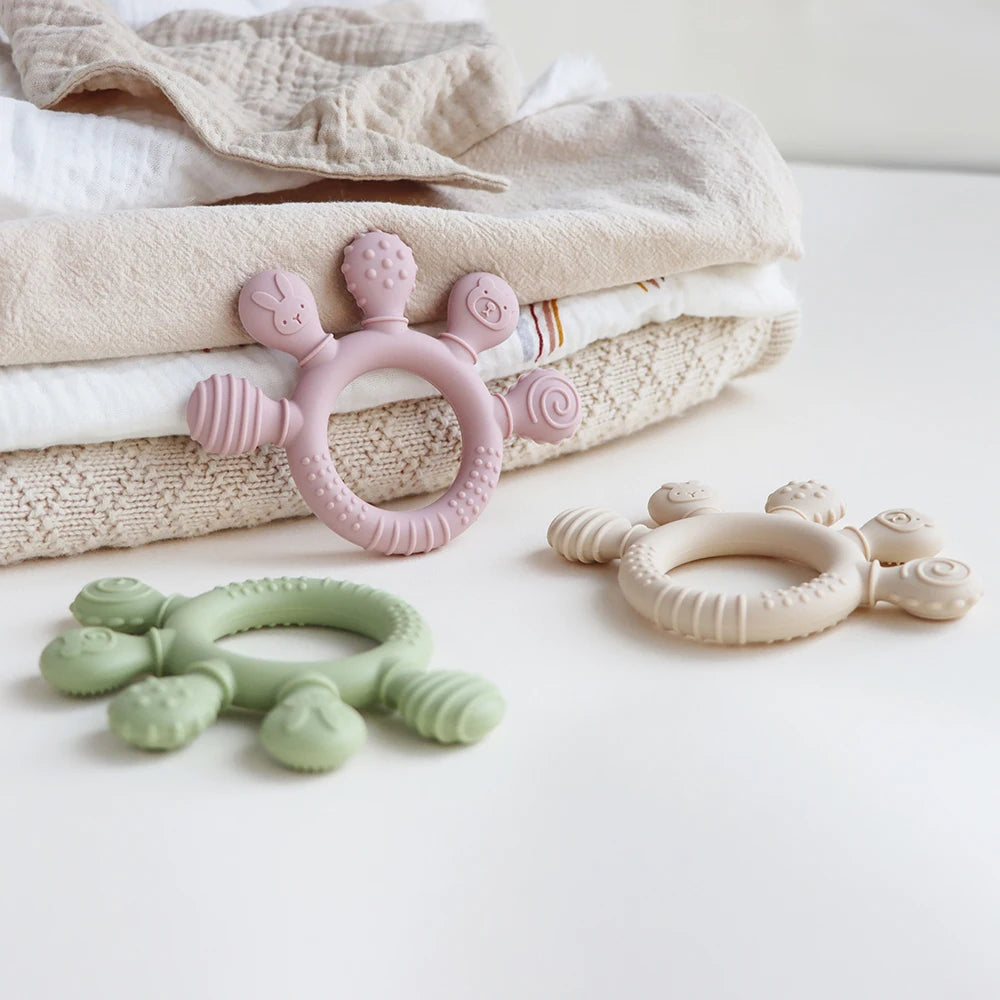 A collection of silicone baby teethers in pink and green resting on a soft, textured cloth.