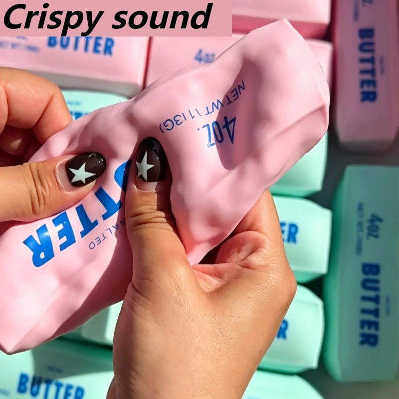 Hands squeezing a pink butter stick squishy stress ball with blue lettering.