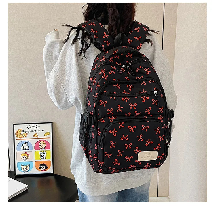 Un sac à dos noir avec motif nœud rouge porté par une personne en pull gris clair.