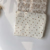 A white muslin swaddle blanket with a floral print is shown folded on a light surface.