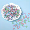 A pile of small, colorful crystal glass mosaic tiles in various shades of green, blue, and pink on a white dish.