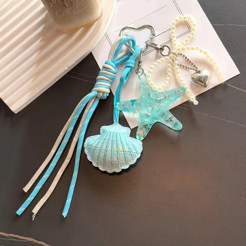 A set of beaded keychains featuring a turquoise starfish and a seashell charm on white and silver cords.