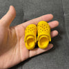A pair of yellow fashion slippers for 1/6 BJD dolls held in a person's hand.