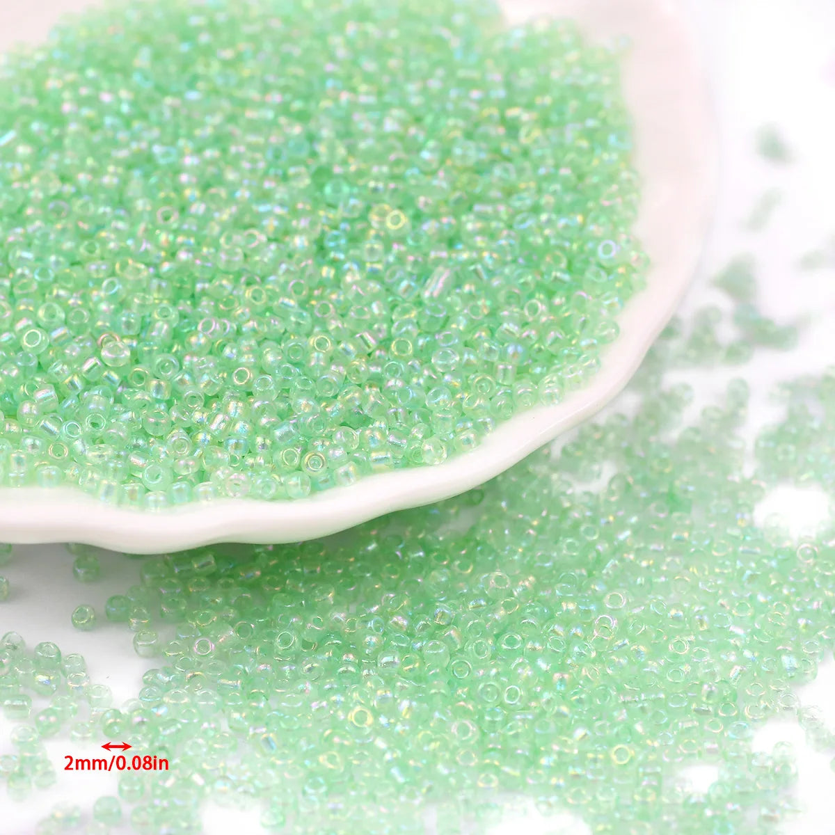 A pile of small, glossy, light green glass seed beads on a white dish and surface.