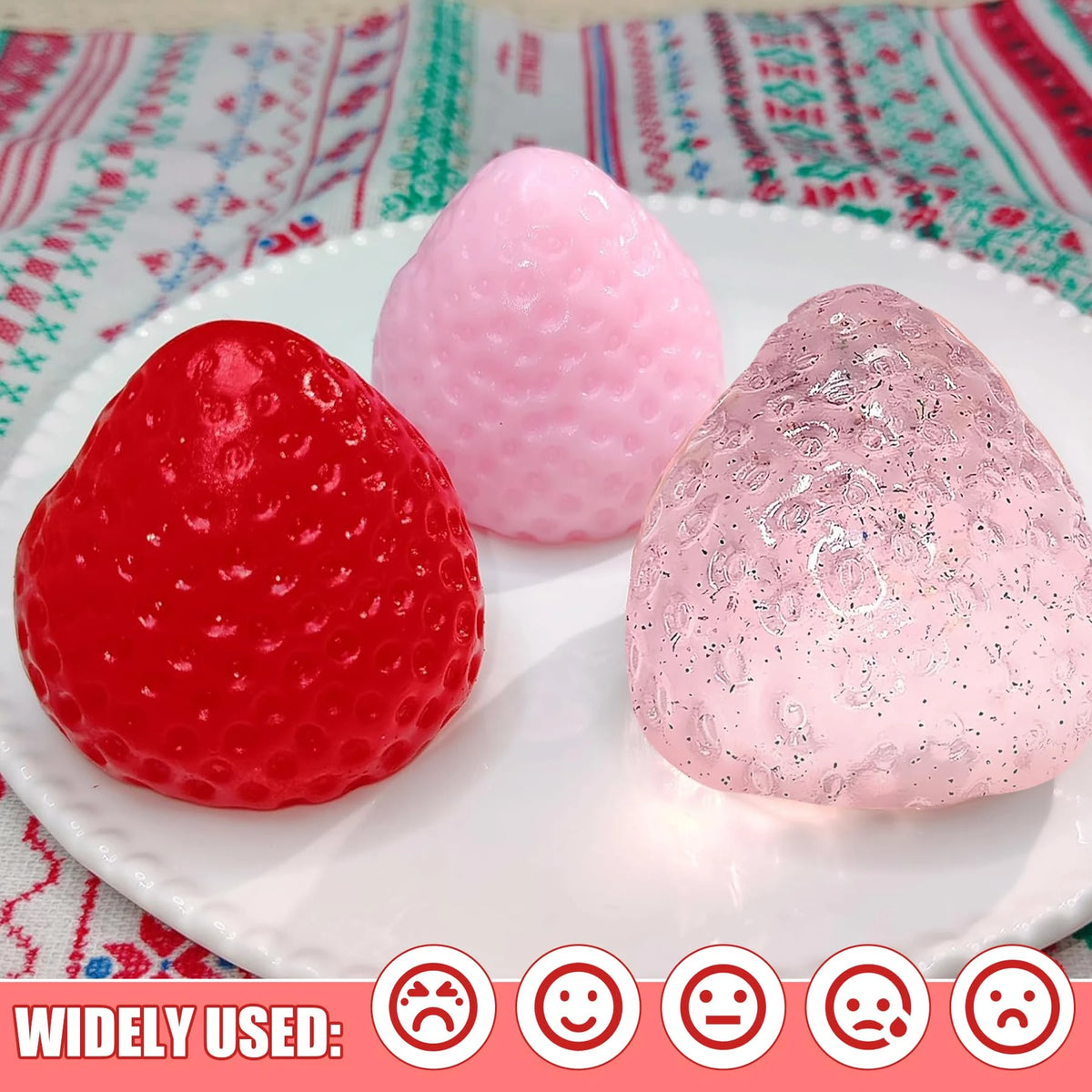 Three squishy toys shaped like strawberries in red, pink, and glitter colors displayed on a white plate.