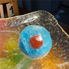 A translucent blue squishy stress relief ball with an orange center resting on a reflective surface.