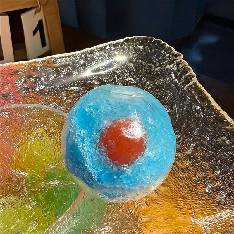 A translucent blue squishy stress relief ball with an orange center resting on a reflective surface.