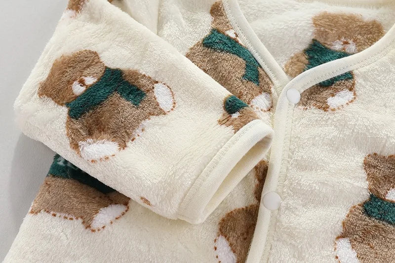 A cream-colored fleece jacket and pants set featuring a brown bear cartoon print with green accents.