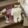 A beige knit ruffle romper and matching bow headband laid out on a wooden surface.