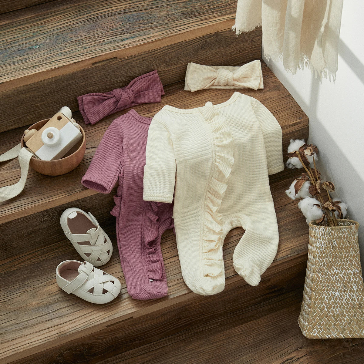 A beige knit ruffle romper and matching bow headband laid out on a wooden surface.