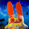 A colorful, fuzzy monster plush doll with large orange ears and pink features.