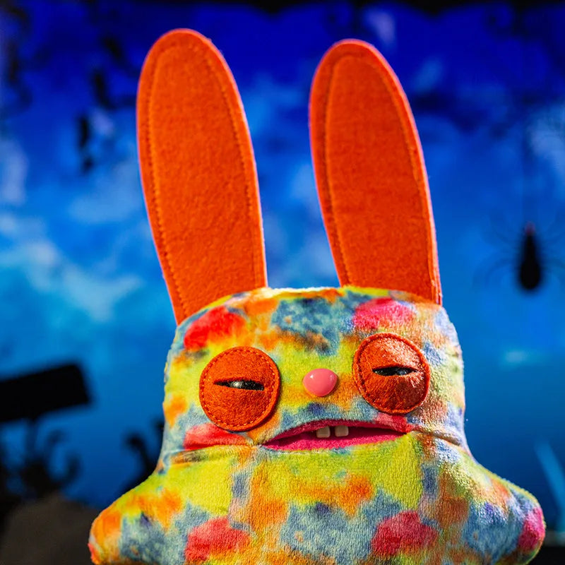A colorful, fuzzy monster plush doll with large orange ears and pink features.