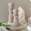Three beige silicone candle molds with twisted ribbed patterns displayed on a wooden slab.