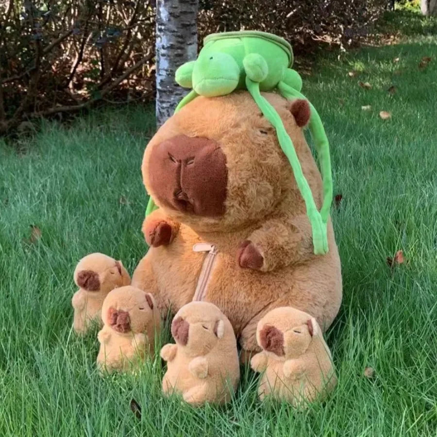 A large brown capybara plush toy with a green head and four smaller baby capybaras surrounding it in green grass.